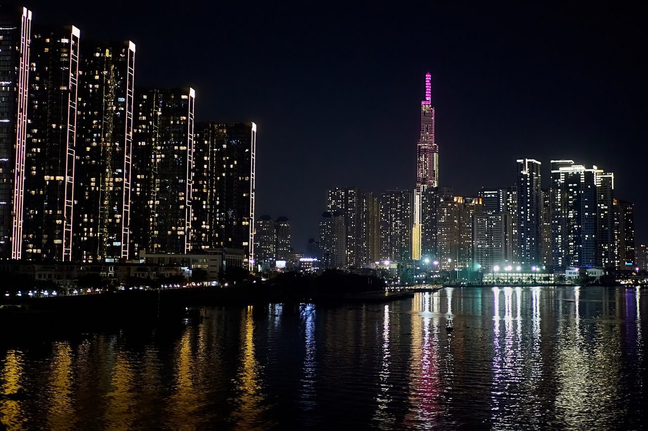 Ночная панорама Хошимина: жилые высотки и подсвеченный небоскрёб Landmark 81 отражаются в реке