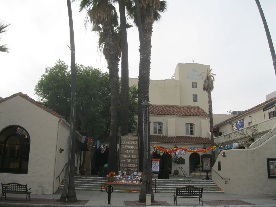 Двор театра в испанском стиле с пальмами, лестницей, вывеской Pasadena Playhouse и скамейками