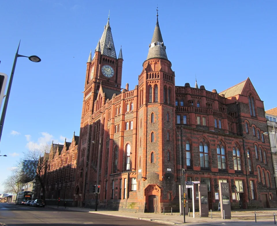 Краснокирпичное здание Victoria Building Ливерпульского университета с часовой башней и шпилями на фоне голубого неба