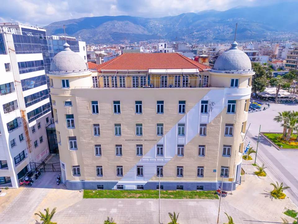 Aerial view of a building with two domes and a red roof against the city and mountains
