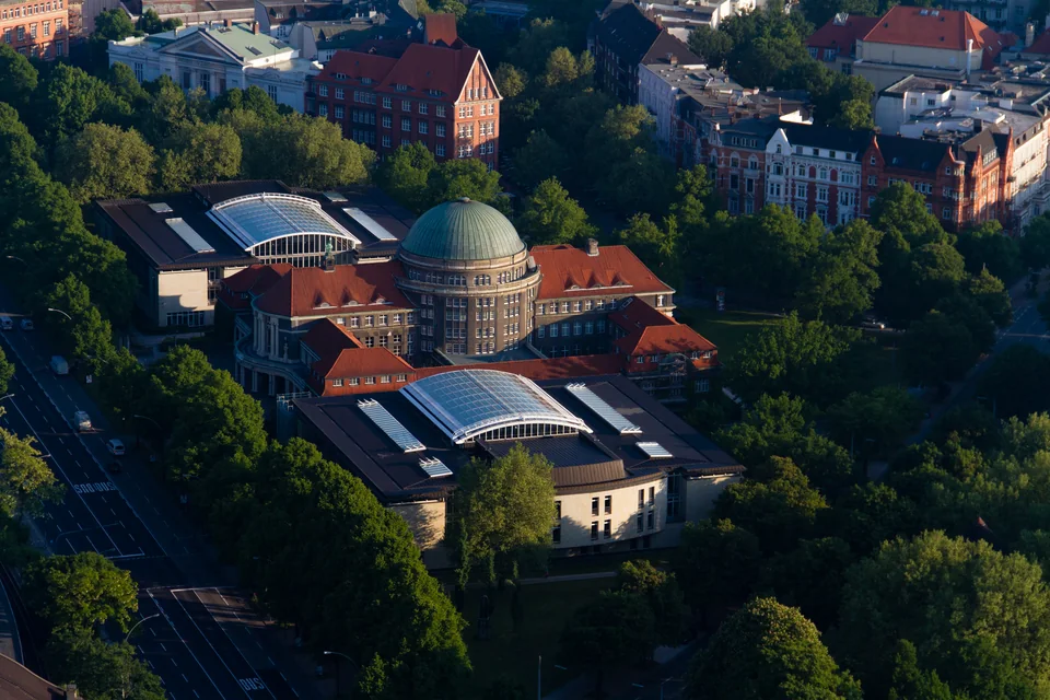 Aerial view of a building with a green dome and glass roofs among trees