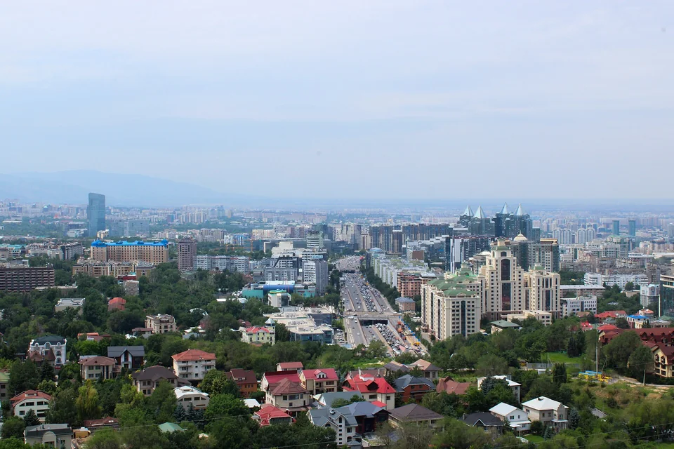 Панорама большого города с холма: частные дома с красными крышами, проспект, многоэтажки и горы в дымке