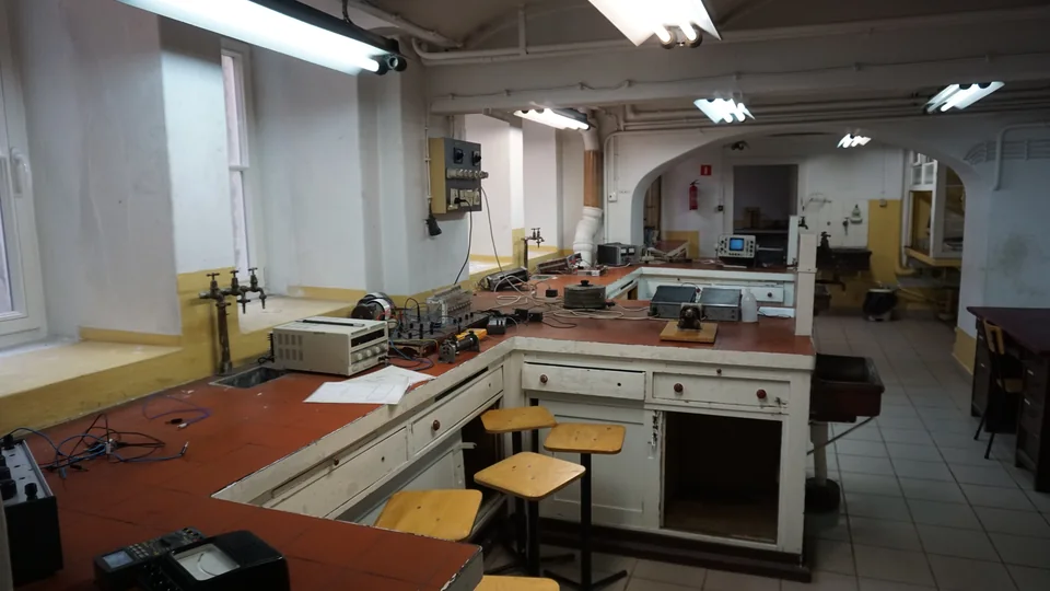 Lab benches with red tiles carrying meters, power supplies and wires, with tall stools alongside