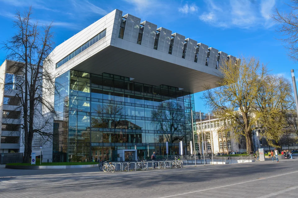 Современное стеклянное здание SuperC университета RWTH Aachen с массивным нависающим верхним объёмом на фоне голубого неба