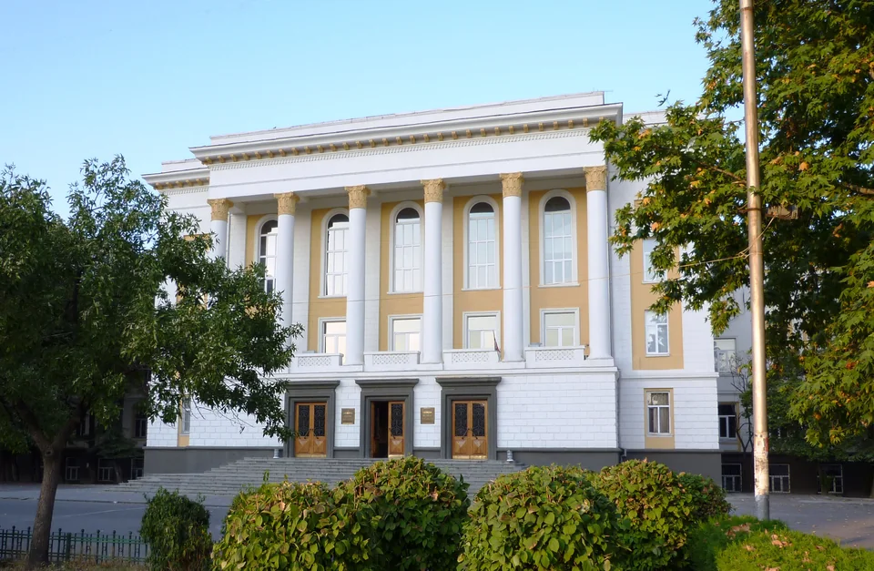 White building with a colonnade and wide steps behind green shrubs