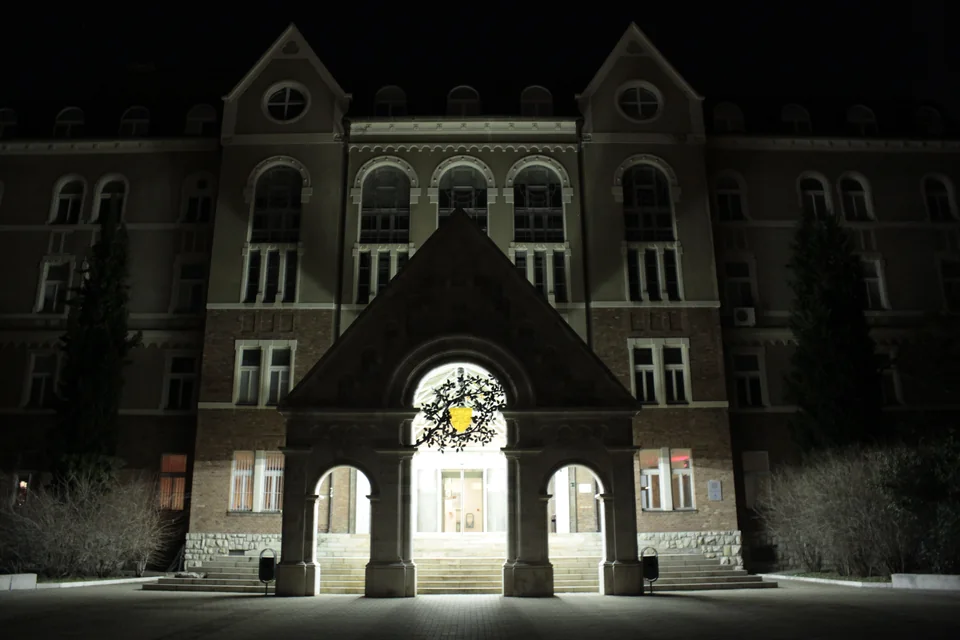 A gabled brick building lit at night, with a stone portal with three arches in front