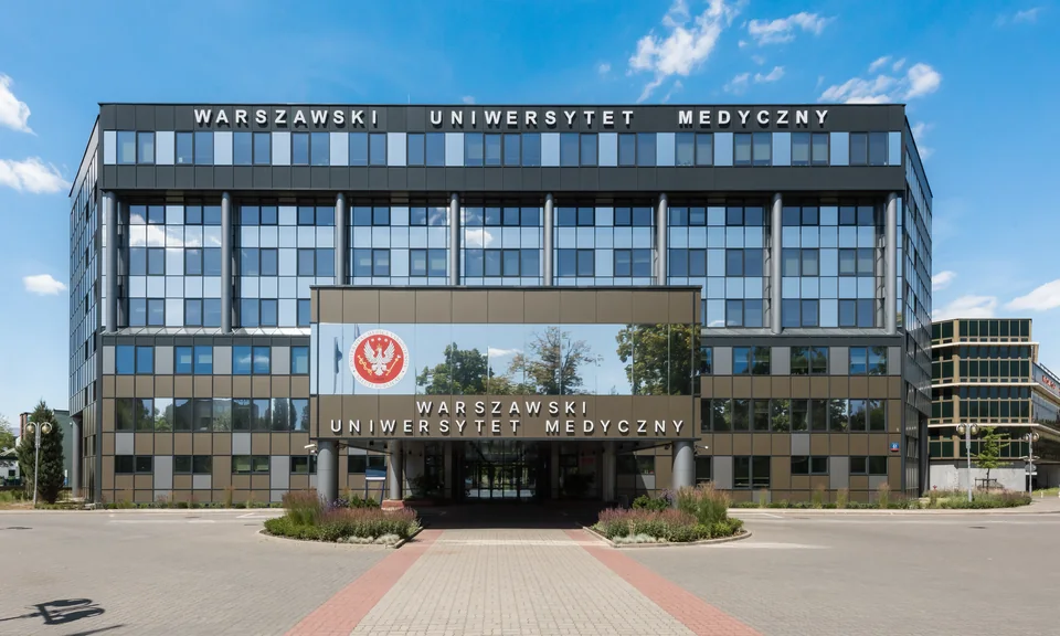 Современное стеклянное здание с надписью «Warszawski Uniwersytet Medyczny» над входом, перед ним мощёная дорожка и клумбы