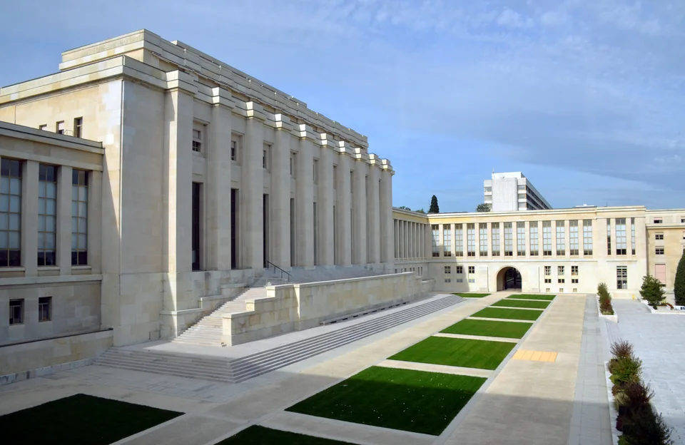 Massive pale stone buildings with a colonnade and broad steps, with strips of lawn in front
