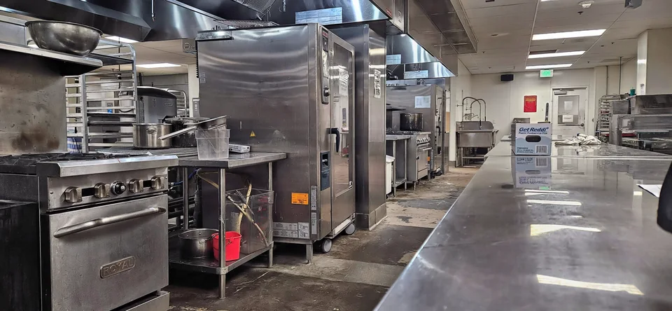 A long row of stainless-steel commercial kitchen equipment along a gleaming worktable, with pots on a range