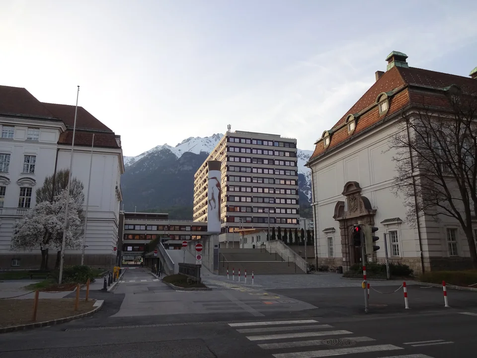 A street between historic university buildings, with a high-rise block and snowy mountains in the distance and a pedestrian crossing in the foreground