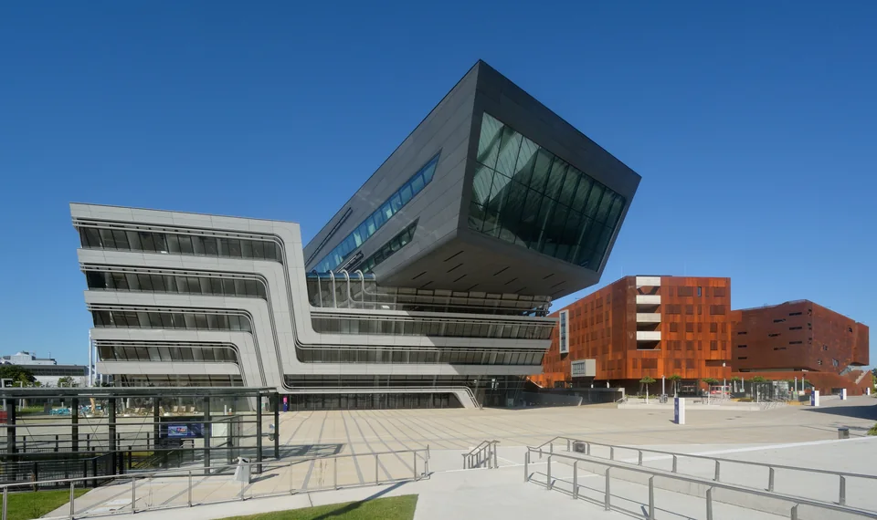 Futuristic building with a tilted dark volume next to a rust-red clad block