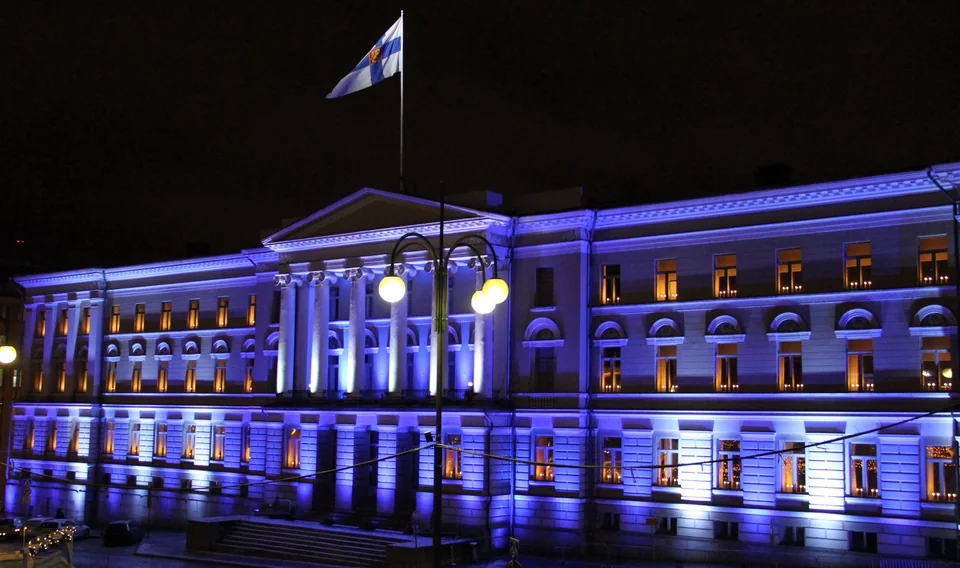 A neoclassical building with a colonnade lit in blue at night, with glowing windows and street lamps