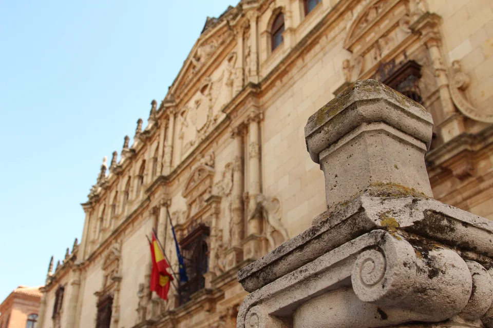 A Renaissance stone façade with carved decoration and flags, shot at an angle, with a stone volute in the foreground