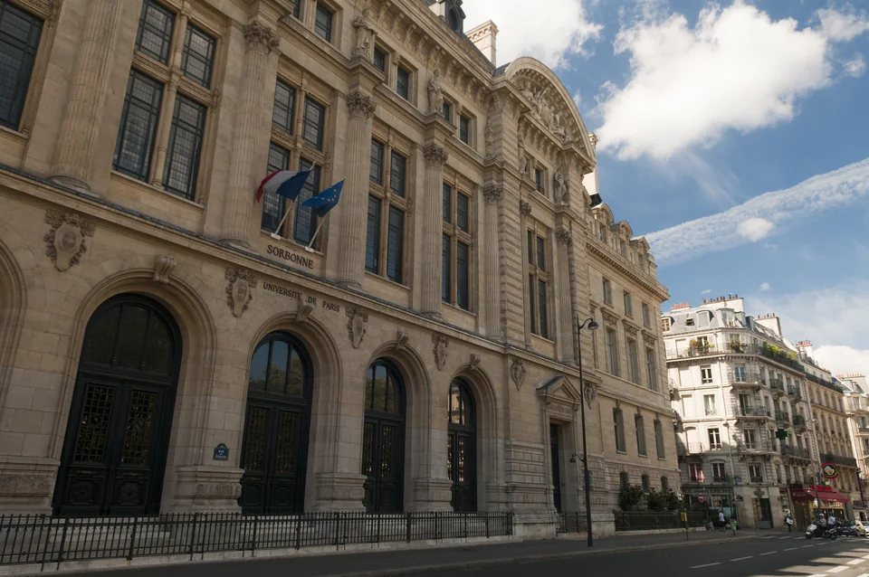 Фасад из светлого камня с надписями Sorbonne и Université de Paris, флагами Франции и ЕС