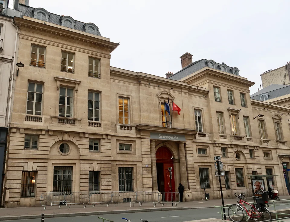 Классический каменный фасад с красной дверью, вывеской SciencesPo и флагами над входом