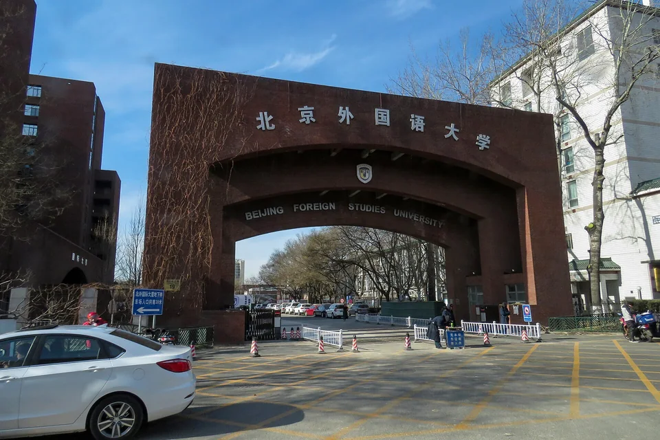 Кирпичная арка ворот с надписью Beijing Foreign Studies University, за ней аллея голых деревьев, ясное небо