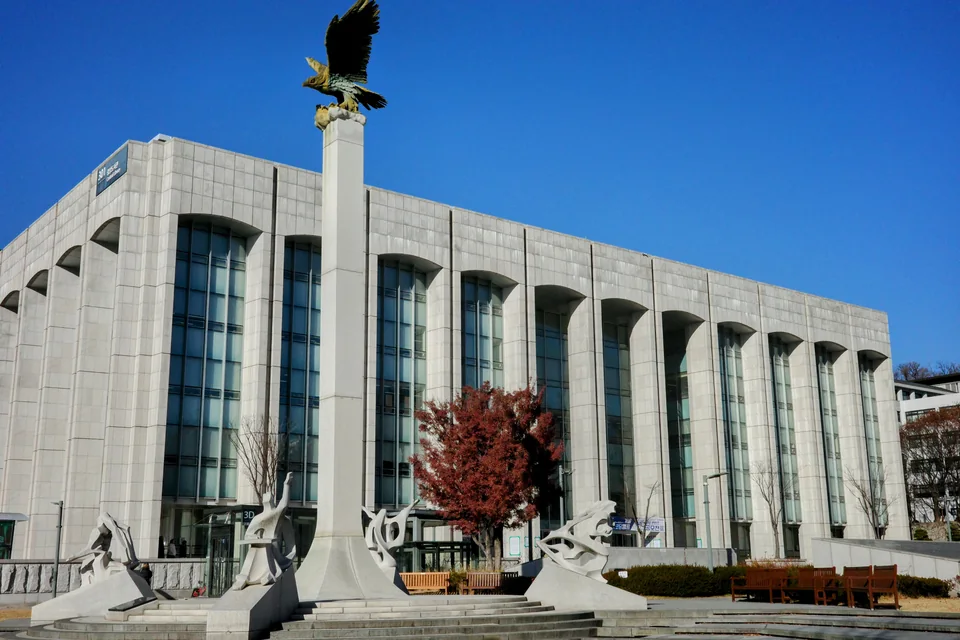 Светлое каменное здание центральной библиотеки Университета Ёнсе с высокими окнами и колонна со статуей орла перед ним