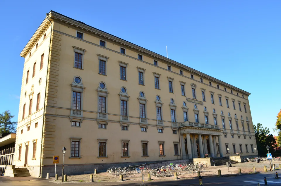 Long yellow building with rows of windows and bicycles by the entrance under a blue sky