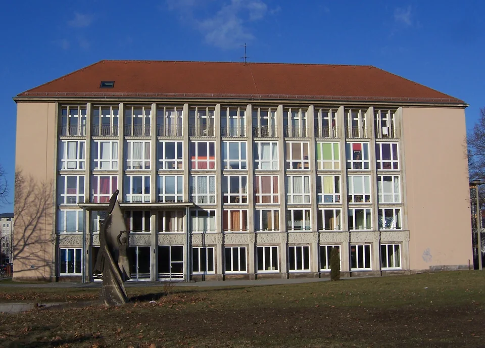 A five-storey residence hall with a grid-like façade and colourful curtains in the windows, with a lawn and a sculpture in front