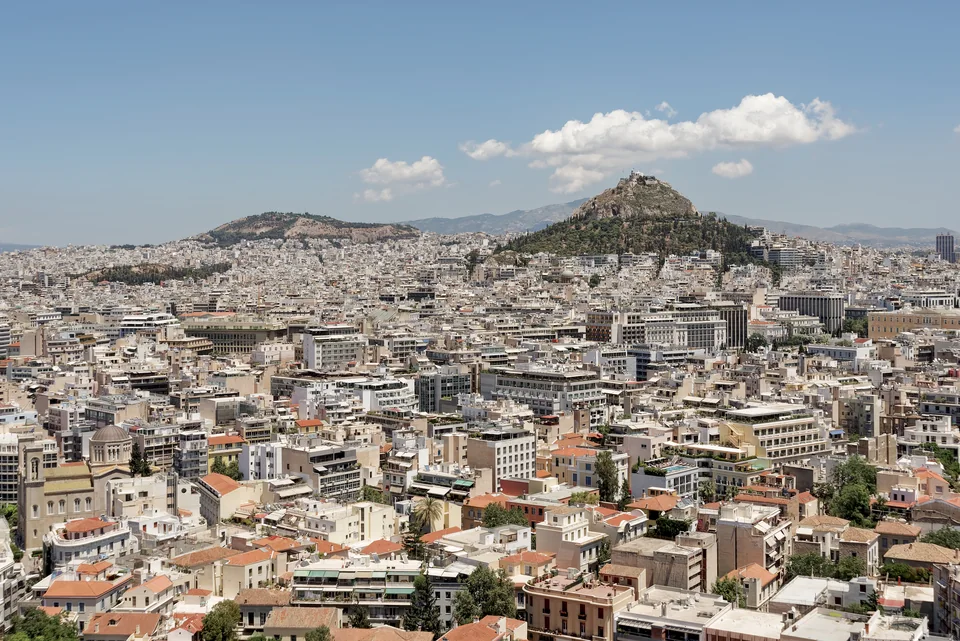 Dense white city blocks to the horizon and a wooded hill with a chapel on top