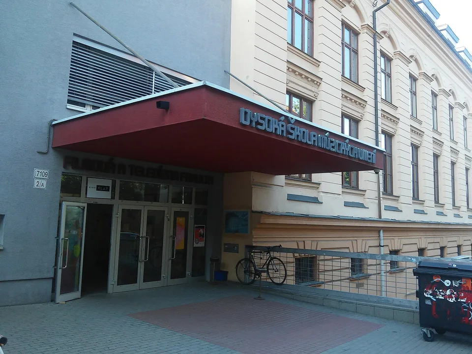 Вход в учебный корпус под красным козырьком с надписью Vysoká škola múzických umení, рядом велосипед у перил