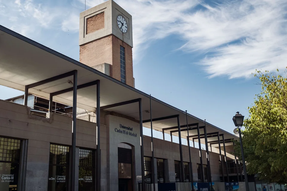 Кирпичная часовая башня над входом с вывеской Universidad Carlos III de Madrid и навесом на металлических опорах