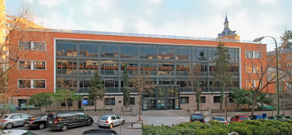Glass facade between brick wings with Universidad CEU San Pablo lettering over the entrance, a car park in front
