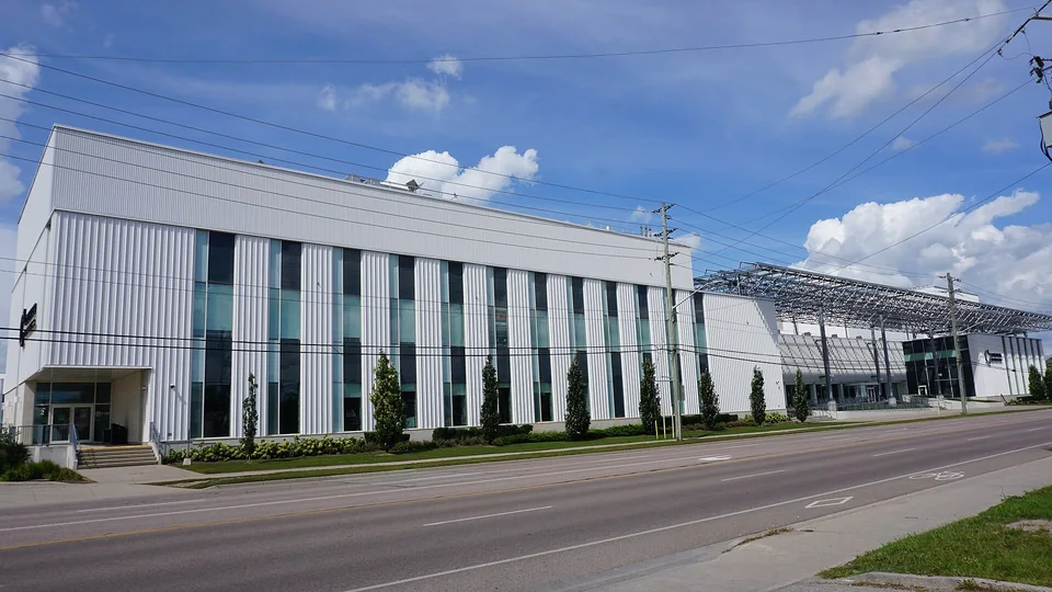 Длинное белое здание кампуса Conestoga College в Ватерлоо с вертикальными окнами и навесом с солнечными панелями вдоль улицы