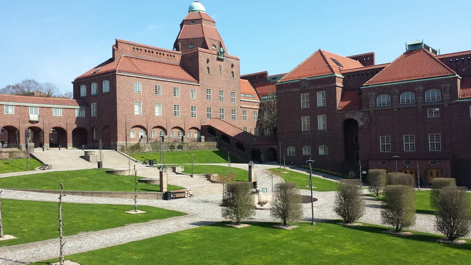 Red-brick buildings with tiled roofs above a courtyard with lawns and steps