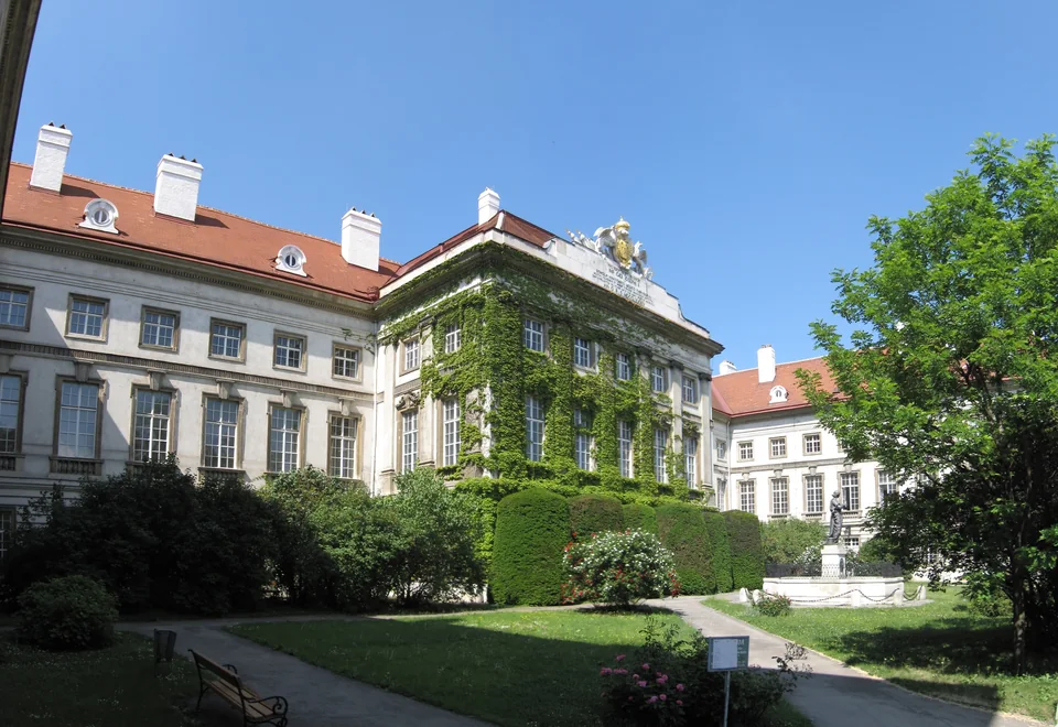 Garden courtyard before a pale red-roofed building, part of the façade covered in ivy