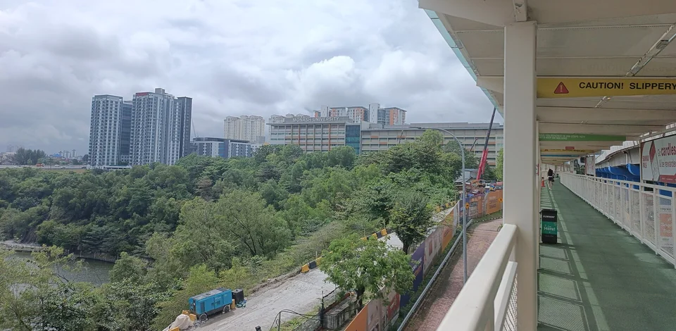 Учебный корпус с надписью Monash University на крыше среди жилых высоток, на переднем плане лесистый склон и крытая пешеходная галерея