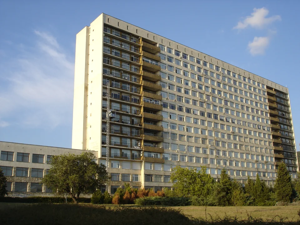 High-rise hospital block with rows of windows and conifers in front