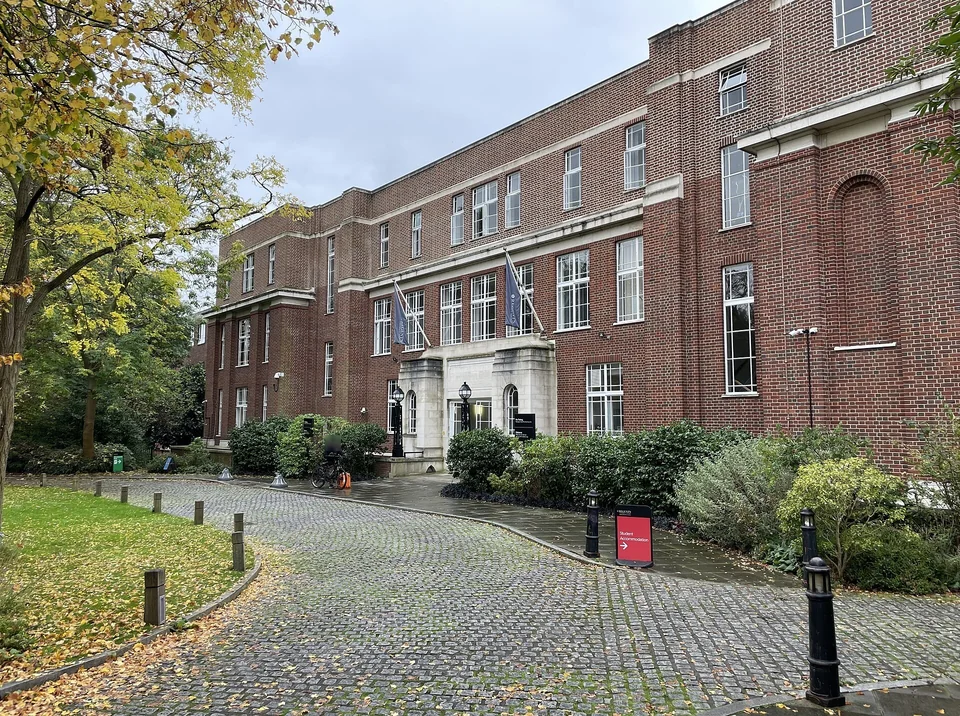Кирпичное здание Herringham Building с флагами над входом и мощёной подъездной дорожкой в осеннем кампусе Regent's University London