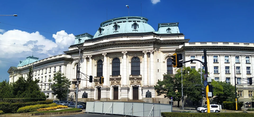 Building with a green dome and columns at a crossroads beside a garden