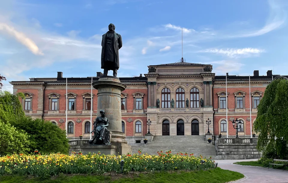 Brick and stone building with a statue on a pedestal and a bed of tulips in front